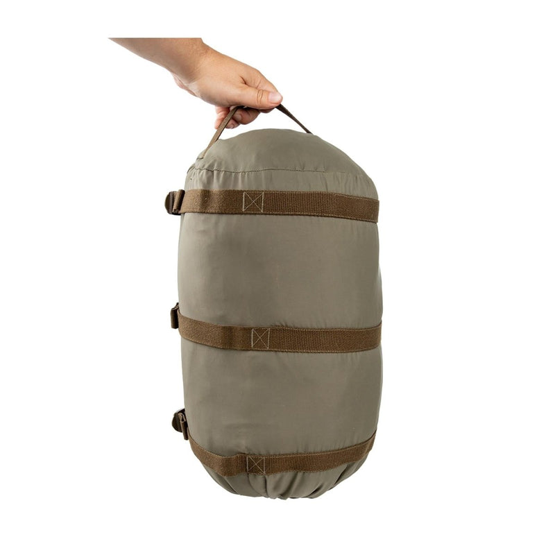 Hand holding an olive green Austrian army compression sack duffel bag for sleeping bag transport