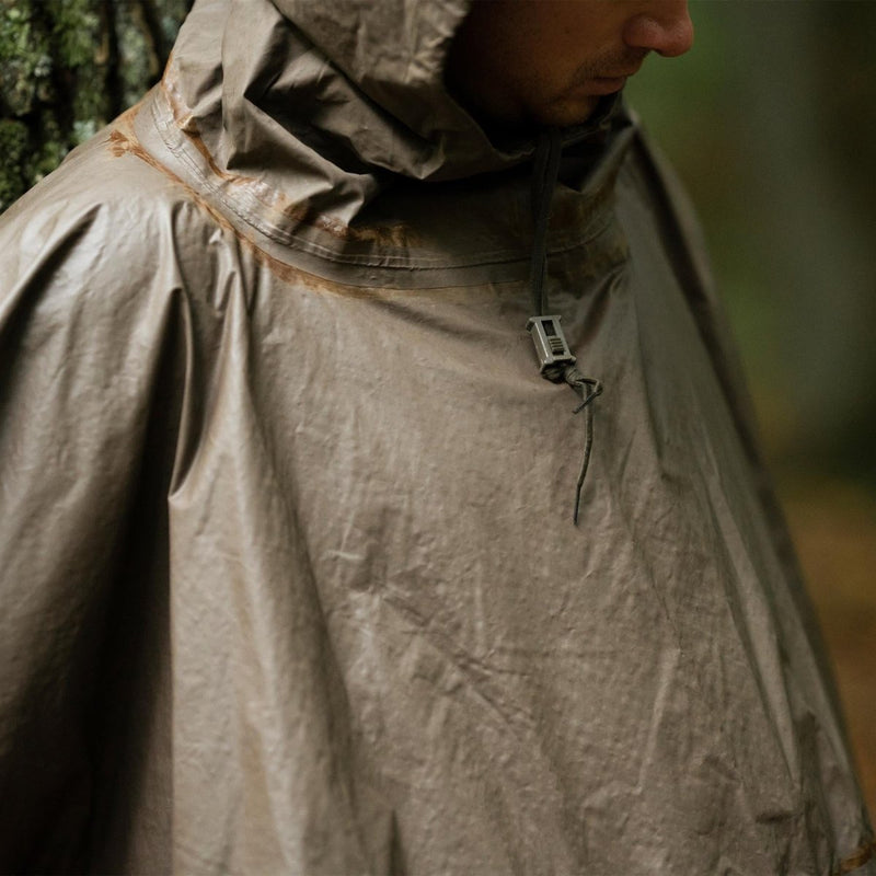 Close-up of a person wearing a vintage German army waterproof olive rain poncho with hood in a forest setting.