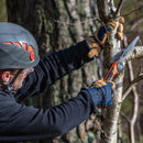 Man wearing safety helmet and gloves using Nordic Pocket Saw to cut a tree branch outdoors