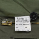 Close-up of a white label with Greek text sewn inside an olive green military field jacket near the zipper and button.