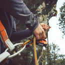 Climber using an orange PETZL GRIGRI+ belay device for assisted braking and rappelling on a rock face outdoors.