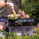 Person cooking outdoors on a portable Primus Onja dual burner camping stove with cookware in natural setting